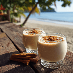 Two glasses of Tios sit on a wooden bench by the ocean. They have cinnamon sprinkled on top and cinnamon sticks sitting next to them.